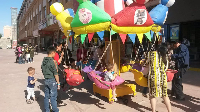 Kinder spielen auf dem Karussell und vor der Kulisse des Hotan-Marktes machen „Hauswächter“ ihre Übungen.